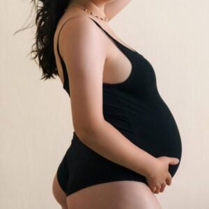 Portrait of a pregnant woman wearing a black bodysuit posing confidently against a neutral background.